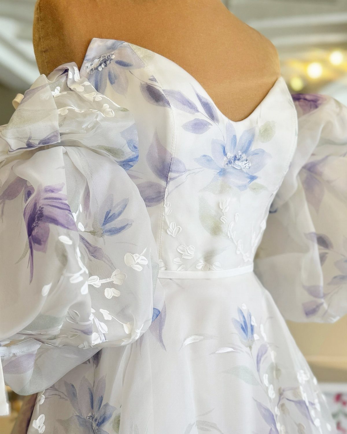 White gown with puffed sleeves and purple floral embroidery on a mannequin