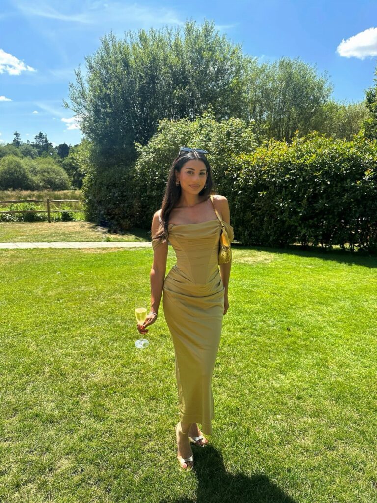 Woman in a gold satin dress holding champagne on a sunny green lawn
