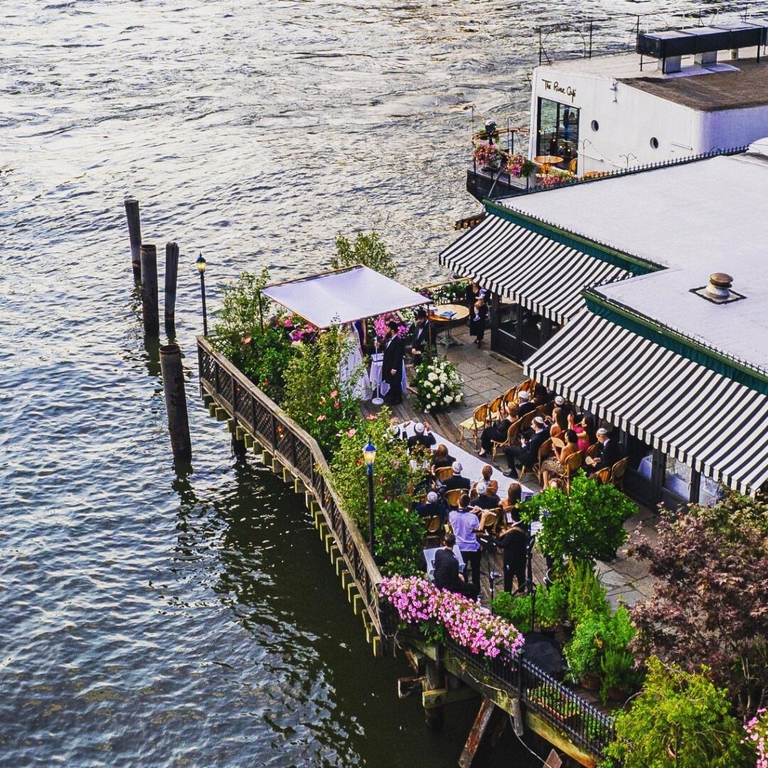 River Cafe waterfront patio with guests dining under striped awnings by the river.