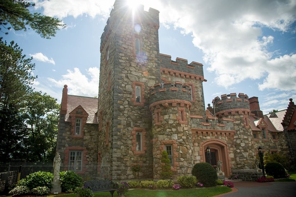 Stone castle with crenelated towers and red brick trim under a sunny sky.
