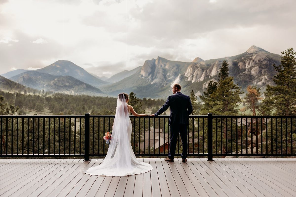 Bride and groom standing on a deck overlooking a scenic mountain range landscape.