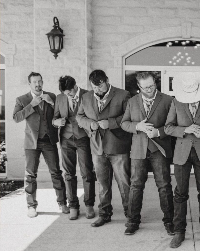 Five men wearing suit jackets and jeans, one with a cowboy hat, outdoors.