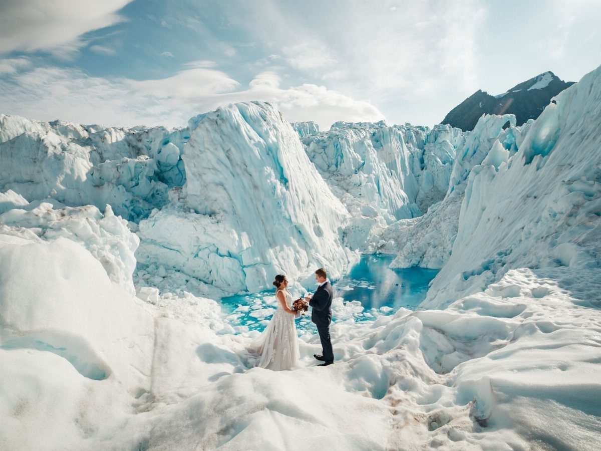 Bride and groom standing together on a massive blue and white glacier landscape.