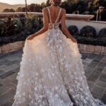Woman in a white floral wedding dress standing on a stone garden patio.