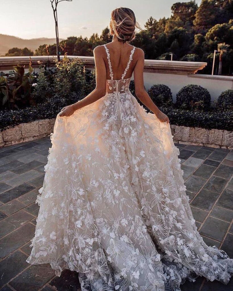 Woman in a white floral wedding dress standing on a stone garden patio.