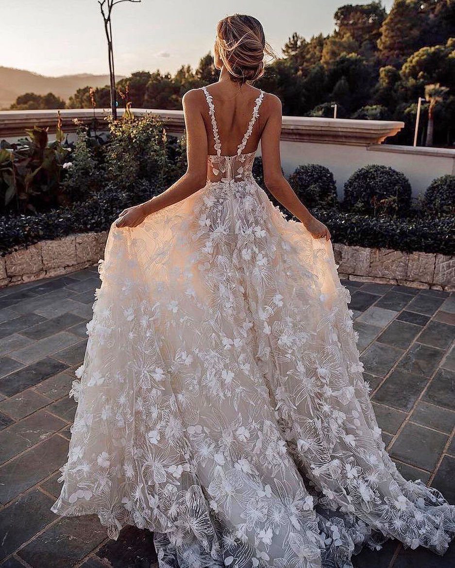 Woman in a white floral wedding dress standing on a stone garden patio.