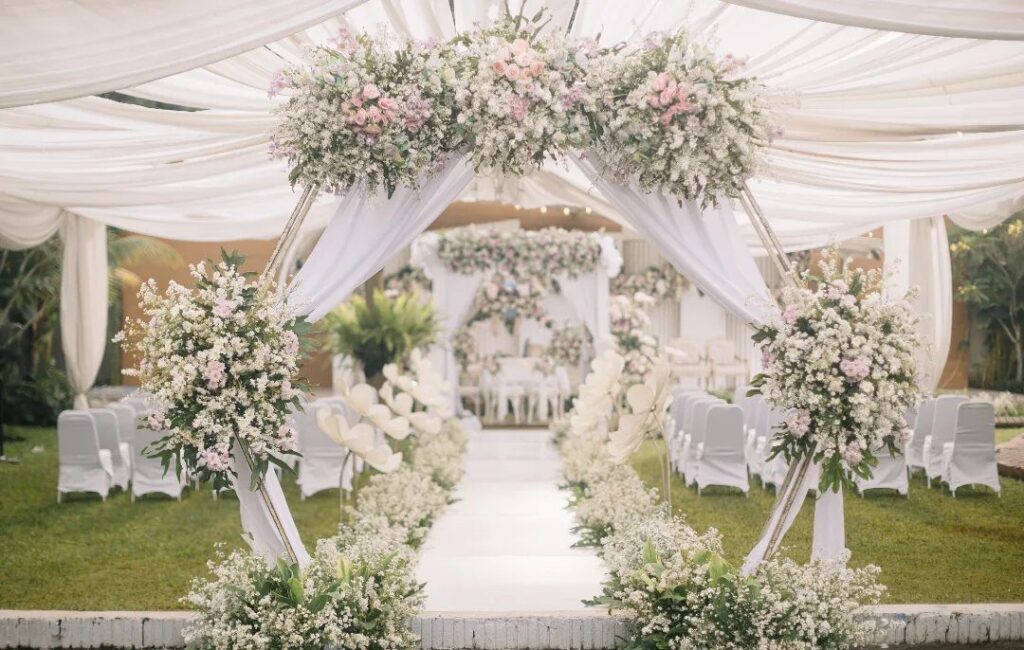 Outdoor wedding ceremony setup with white fabric draping and pink floral arrangements.