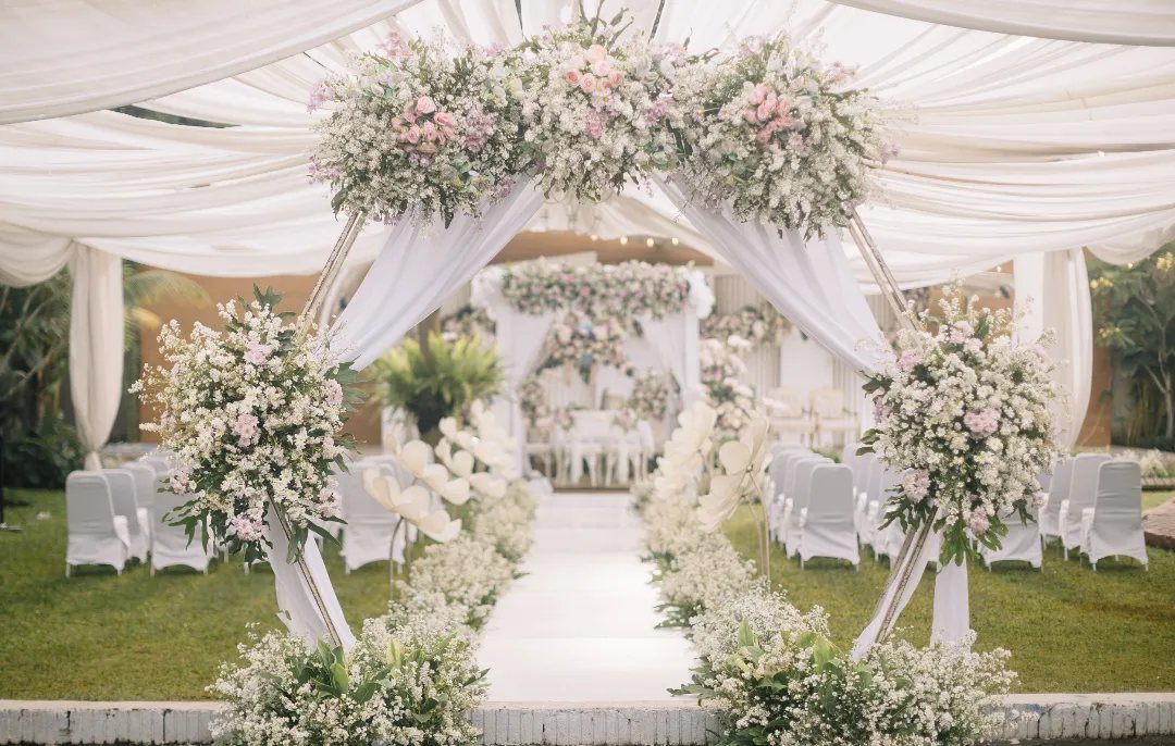 Outdoor wedding ceremony setup with white fabric draping and pink floral arrangements.