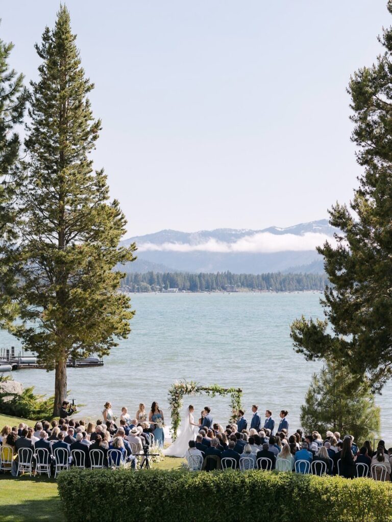 Wedding ceremony with a floral arch on a lawn overlooking Lake Tahoe mountains.