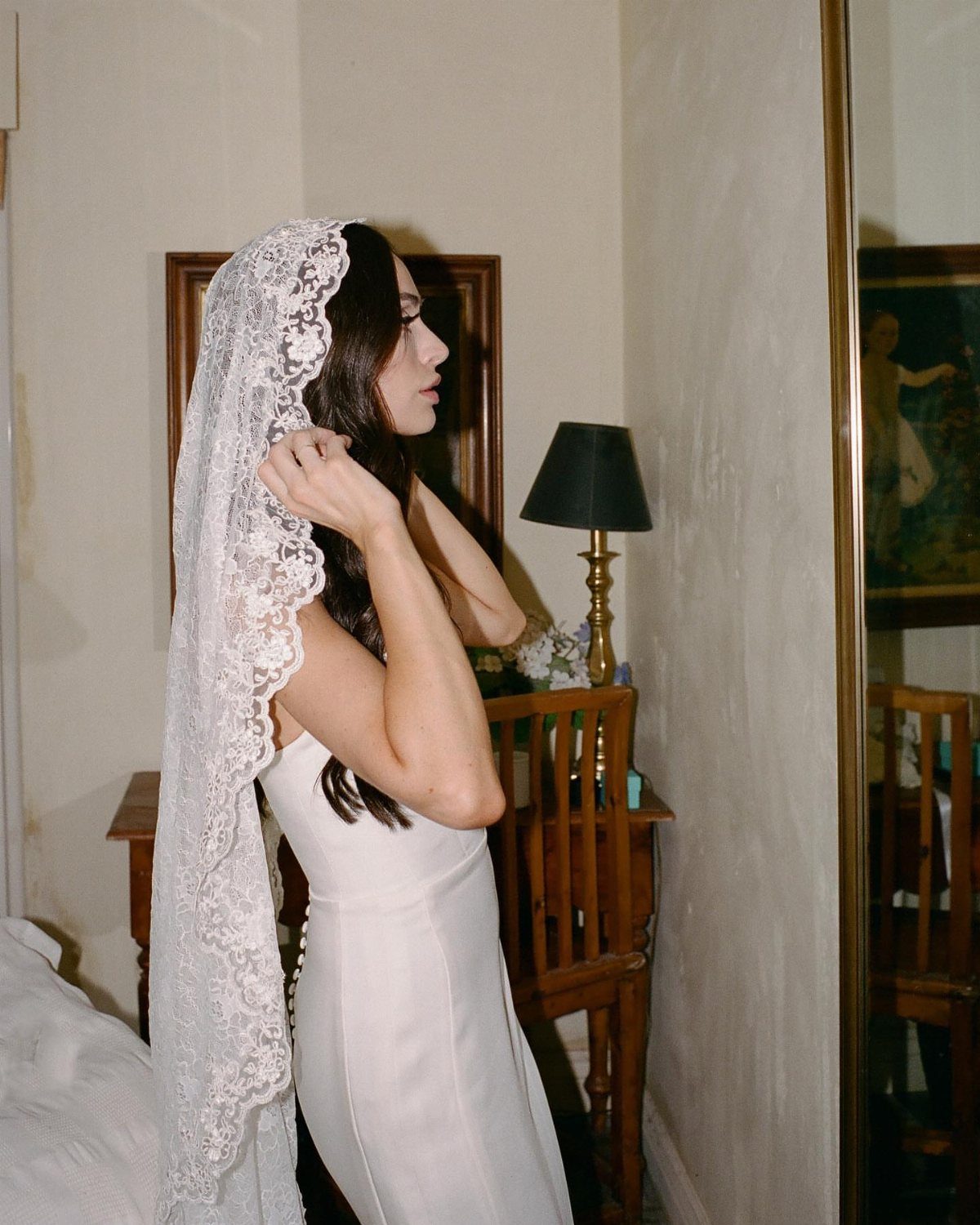 Woman in a white wedding dress wearing a long lace mantilla veil.