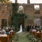 Wedding ceremony in brick ruins with a floral arch and guests in pews