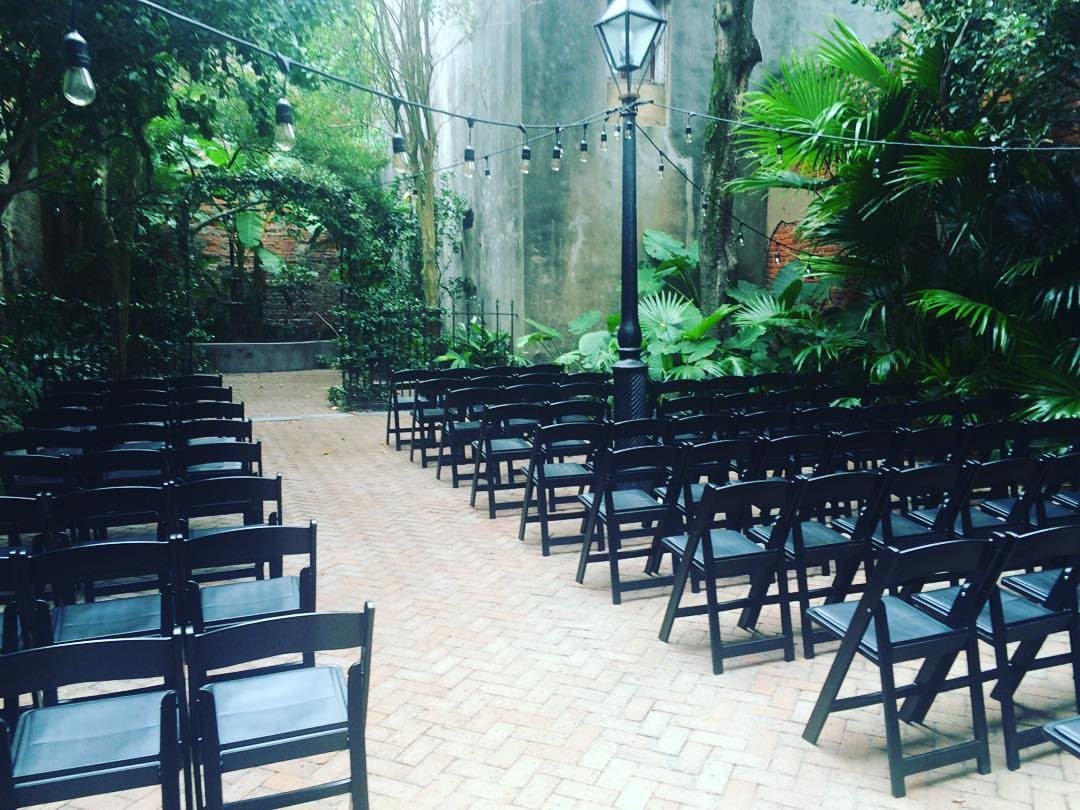 Outdoor courtyard with black folding chairs, brick flooring, and lush tropical greenery.