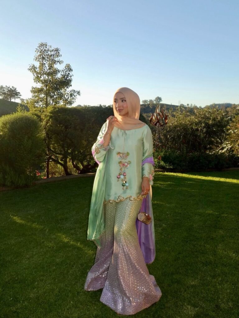 Woman in a pastel green tunic and shimmering purple sequined skirt standing outdoors.