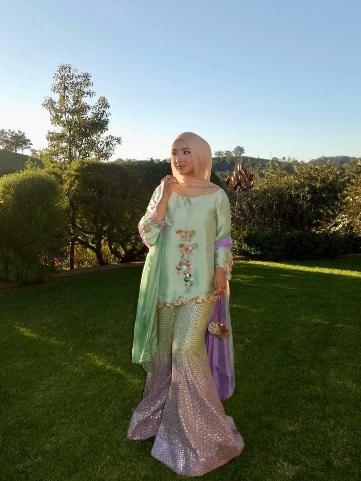 Woman in a pastel green tunic and shimmering purple sequined skirt standing outdoors.