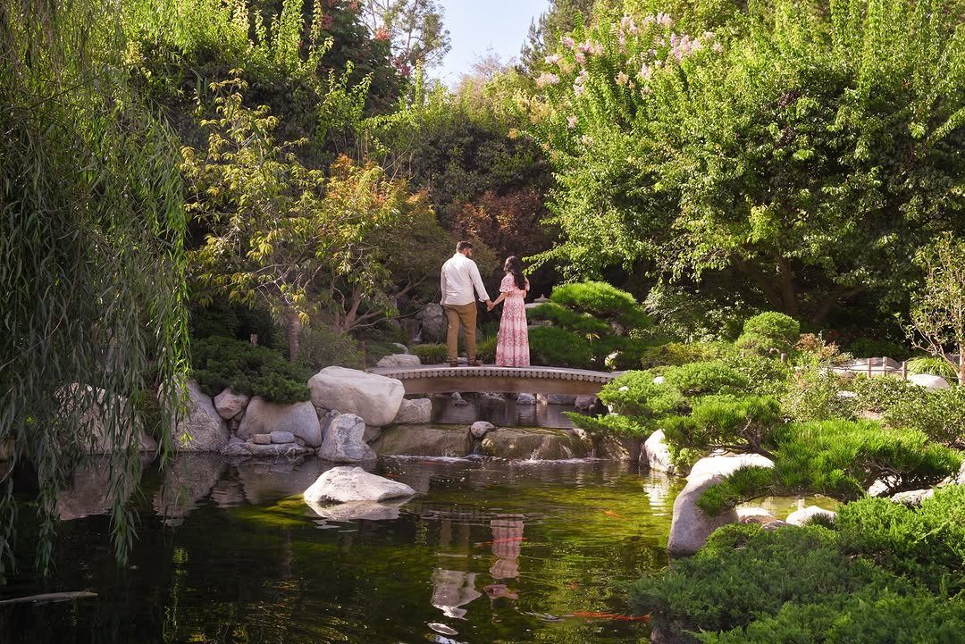 Couple standing on a stone bridge in a serene Japanese garden with a pond.