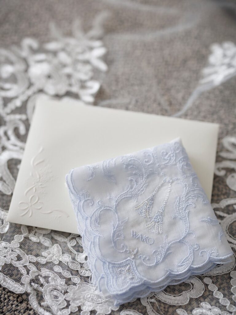 Light blue lace handkerchief resting on a white envelope and white lace fabric.