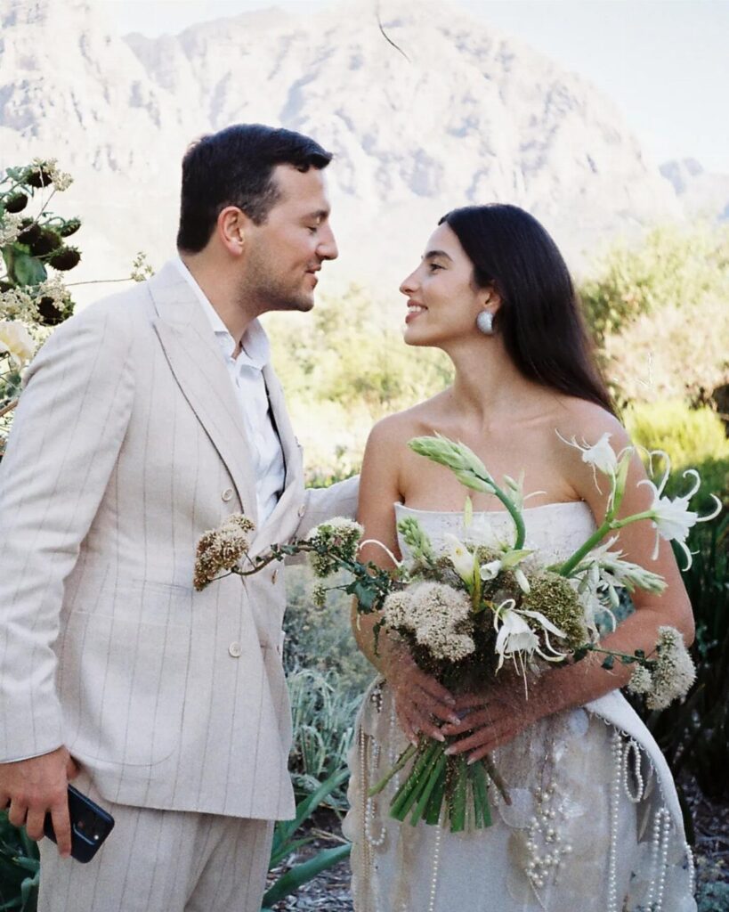 Couple in wedding attire facing each other with mountains in the background.