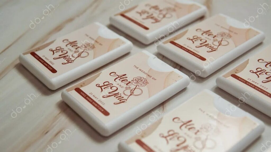 Small white hand sanitizer bottles with custom wedding labels on a marble surface.