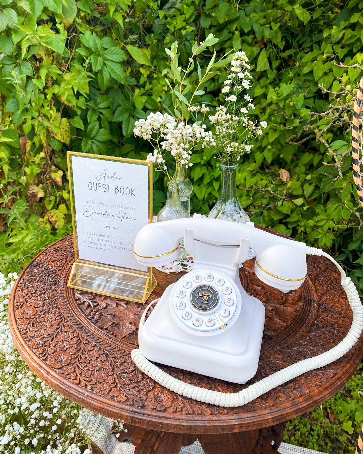 White vintage rotary phone and guest book sign on a carved wooden table.