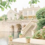 Stone manor house with arched bridge and stairs by a calm river