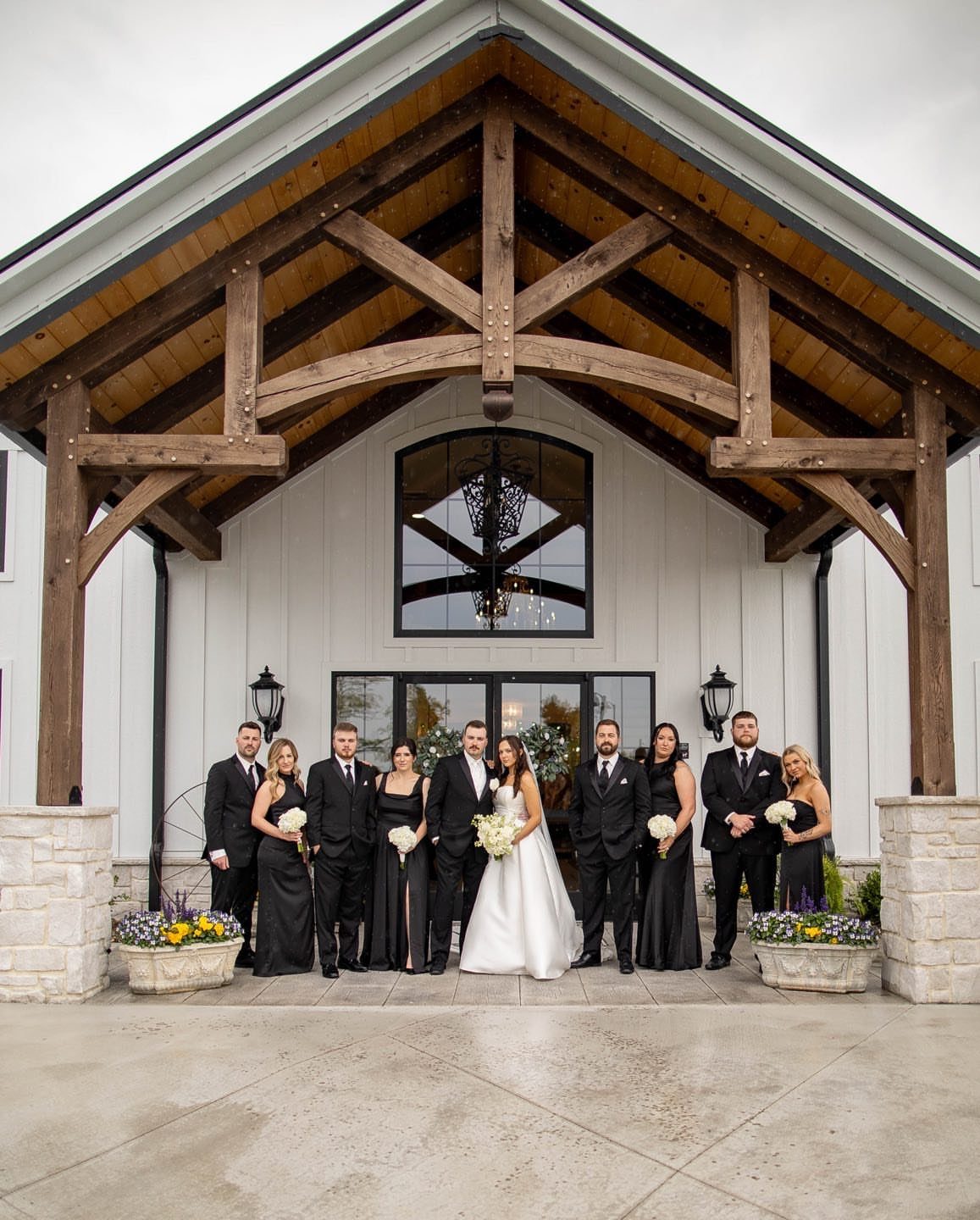 Wedding party posing under a rustic wooden timber porch at a barn venue.