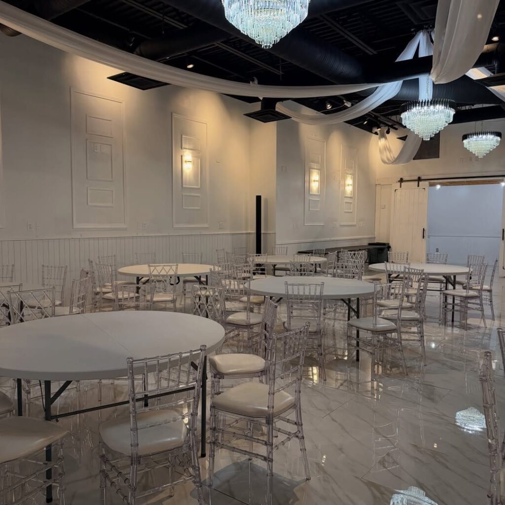 Elegant event venue with round white tables, clear chairs, and crystal chandeliers.