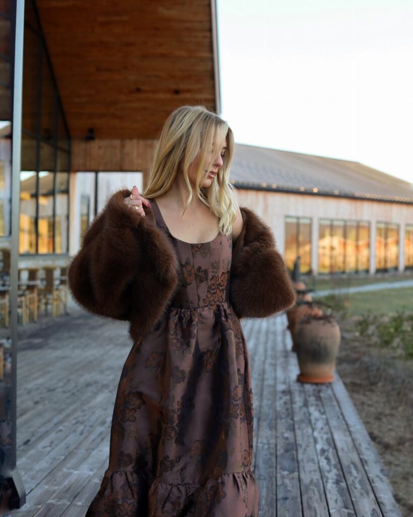 Blonde woman in a brown floral winter wedding guest dress and fur shrug.